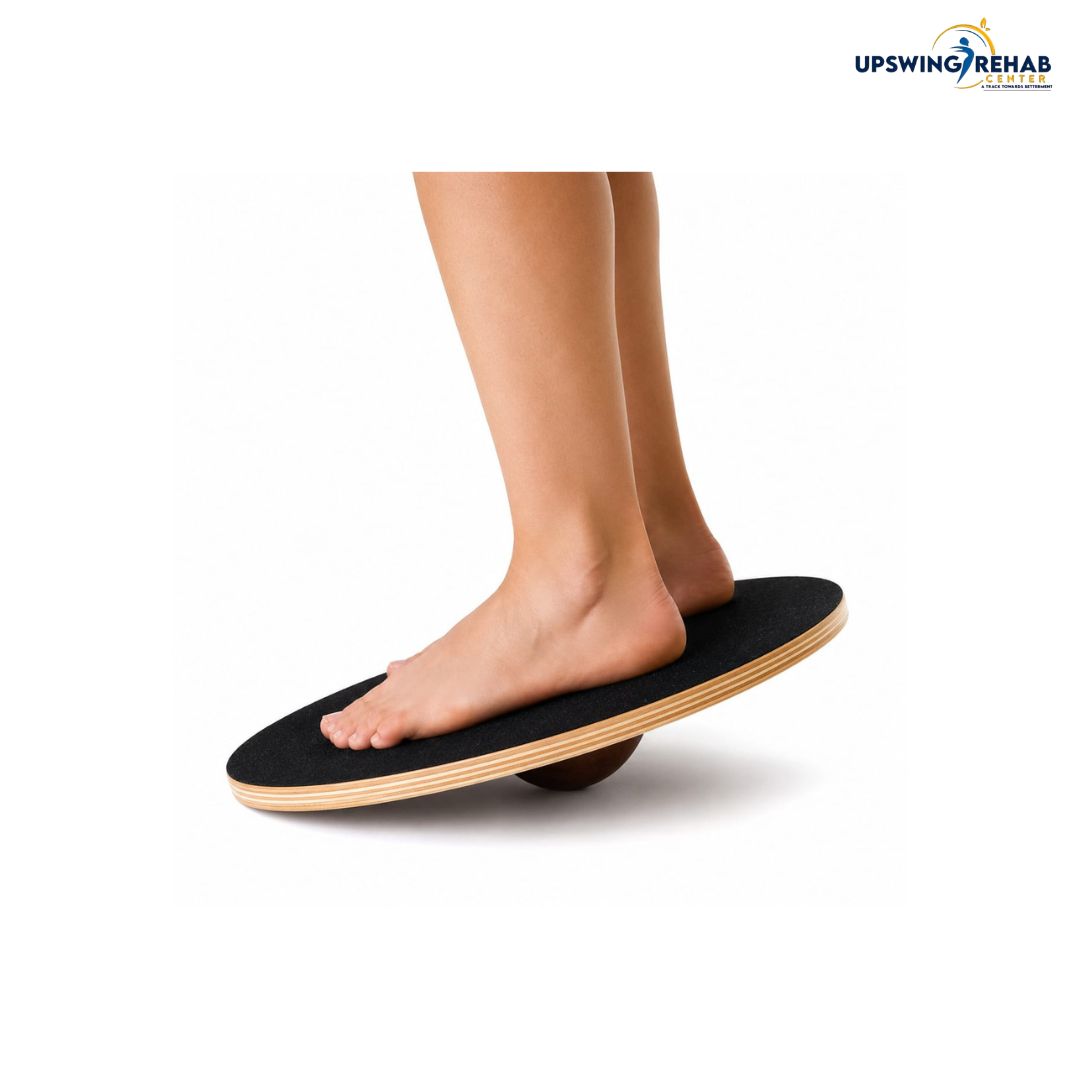 A person's bare feet and lower legs are balancing on a black and wood balance board against a white background, with the UPWING REHAB logo in the top right corner.